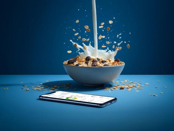 milk poured into a bowl with breakfast cereal, with a mobile phone showing the DeLaval Plus dashboard.
