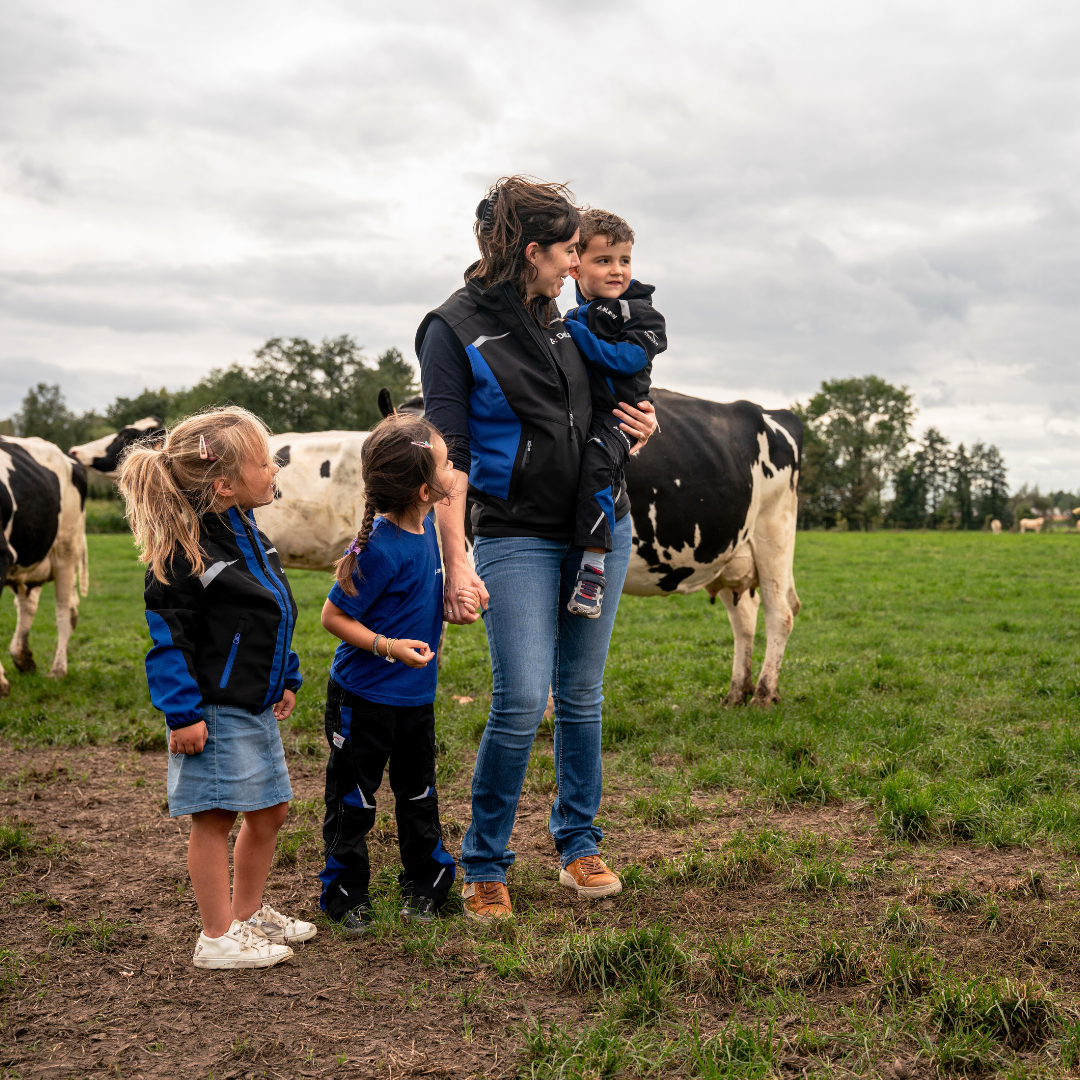 Vrouw met 3 kinderen in een weiland met koeien. Ze dragen DeLaval kleding