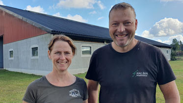 Lantbrukarna Karin och Sven Nalbin står i kortärmat framför stallbyggnaden en sommardag
